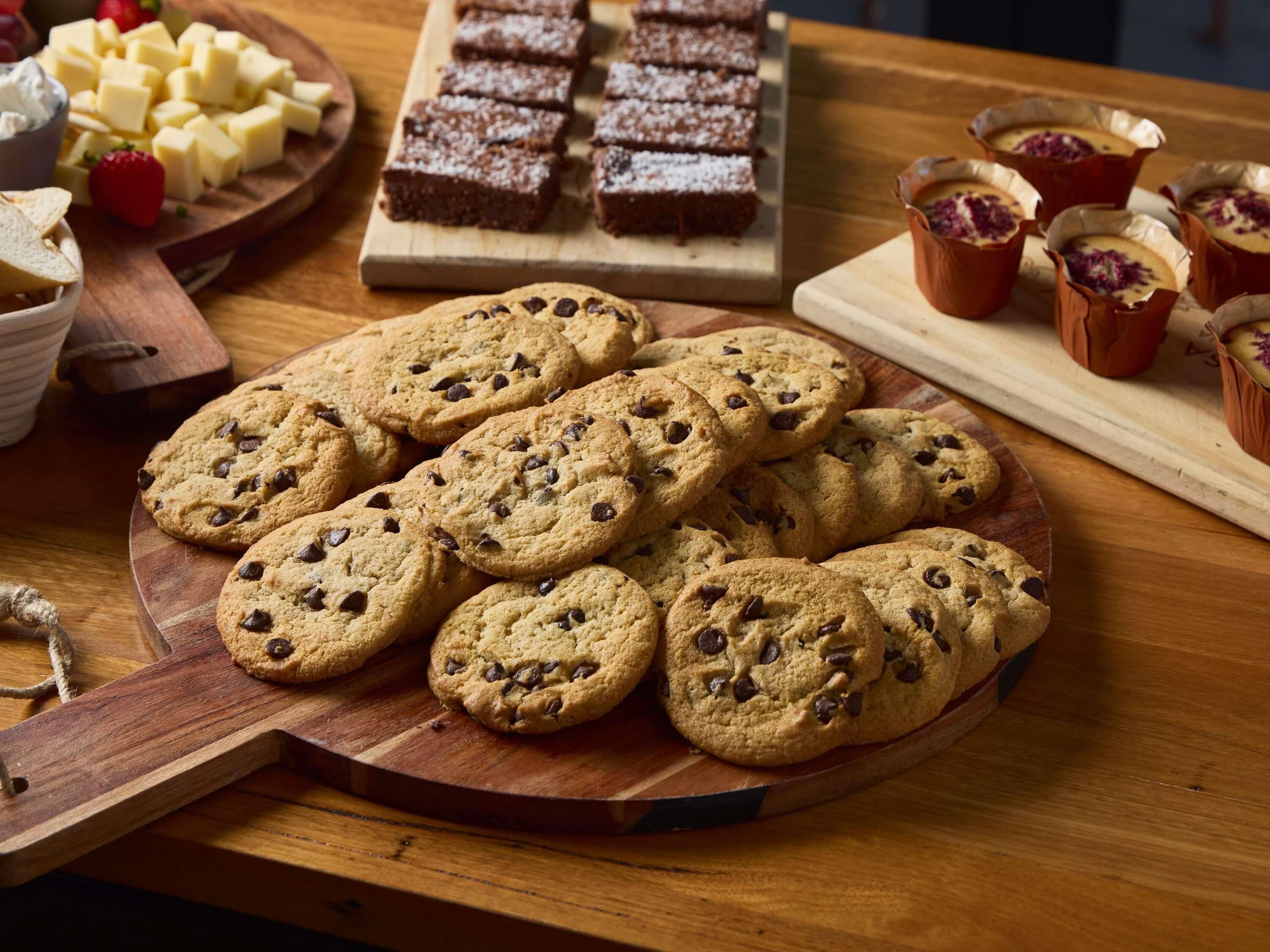 A wooden table with a variety of baked goods including cookies, brownies, and custard cups.