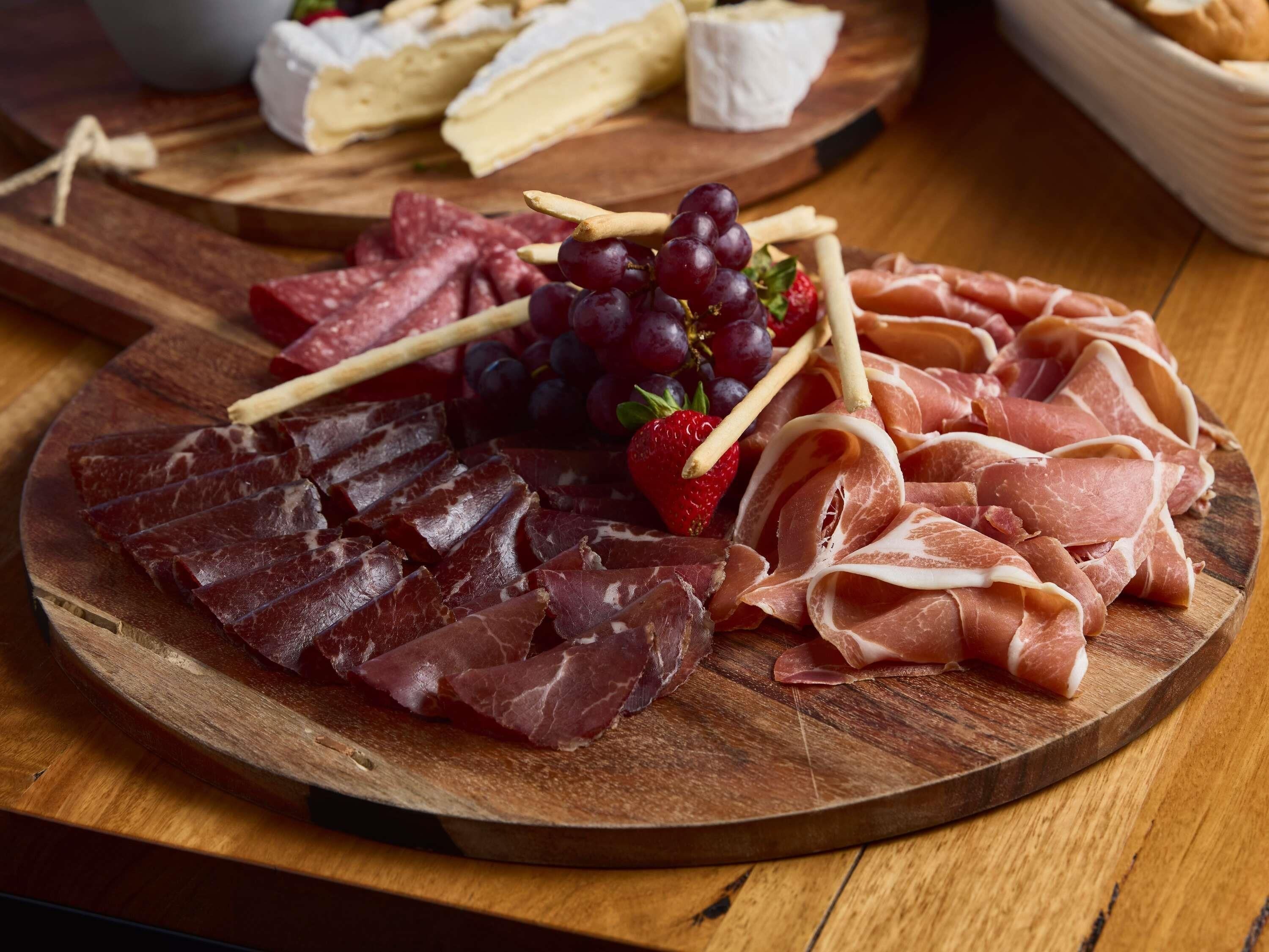 Uma tábua de madeira com diversos carnes, uvas e uma morango.