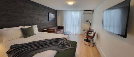 A modern hotel room with a large bed, a green sofa, a small table, and a TV mounted on the wall.