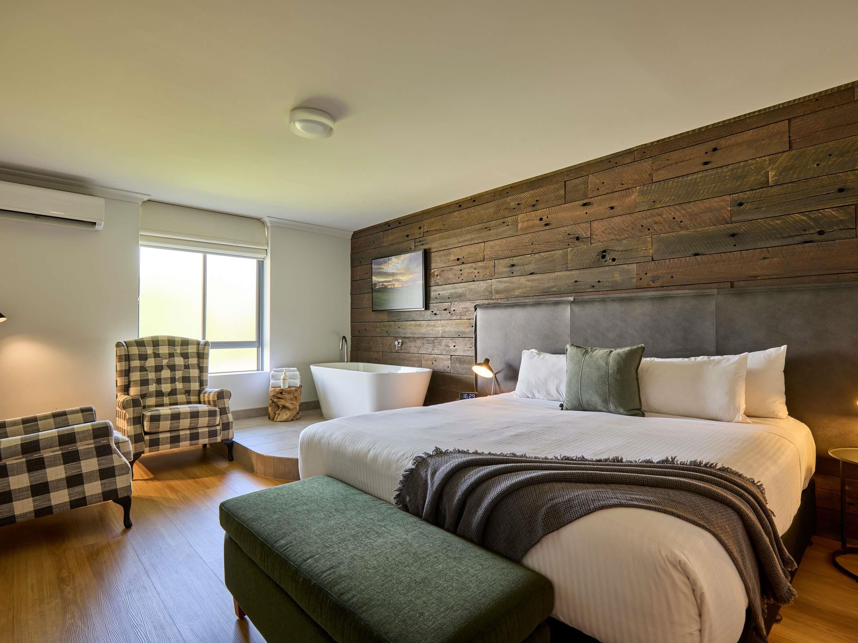 A modern bedroom with a large bed, a wooden accent wall, a checkered armchair, and a small side table.