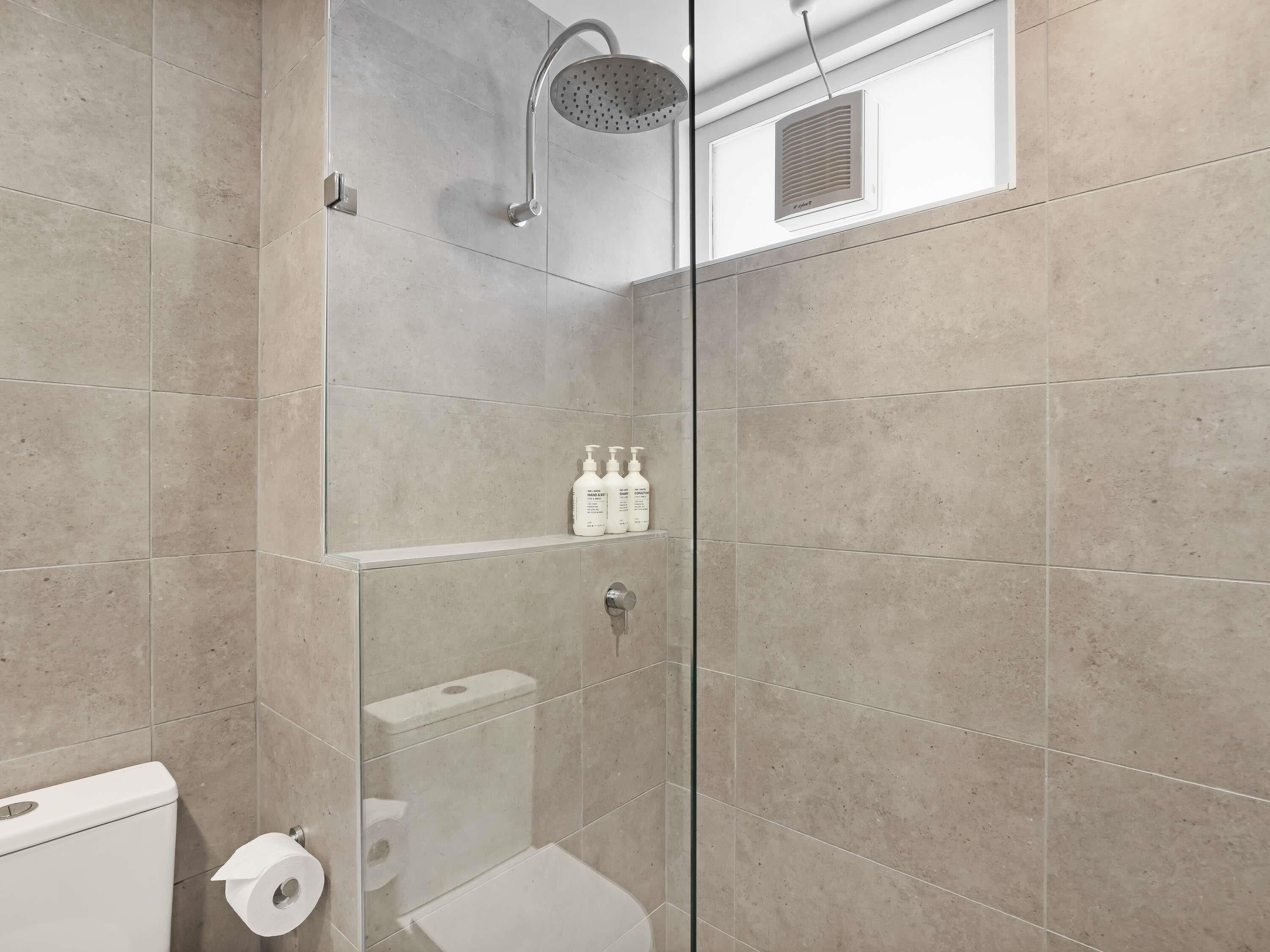 A modern bathroom with a glass shower enclosure, a toilet, and a shelf with toiletries.
