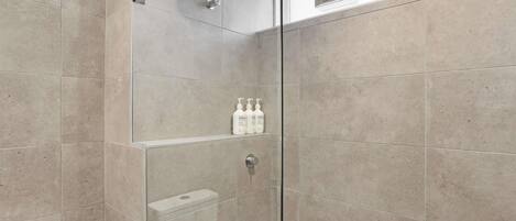 A modern bathroom with a glass shower enclosure, a toilet, and a shelf with toiletries.