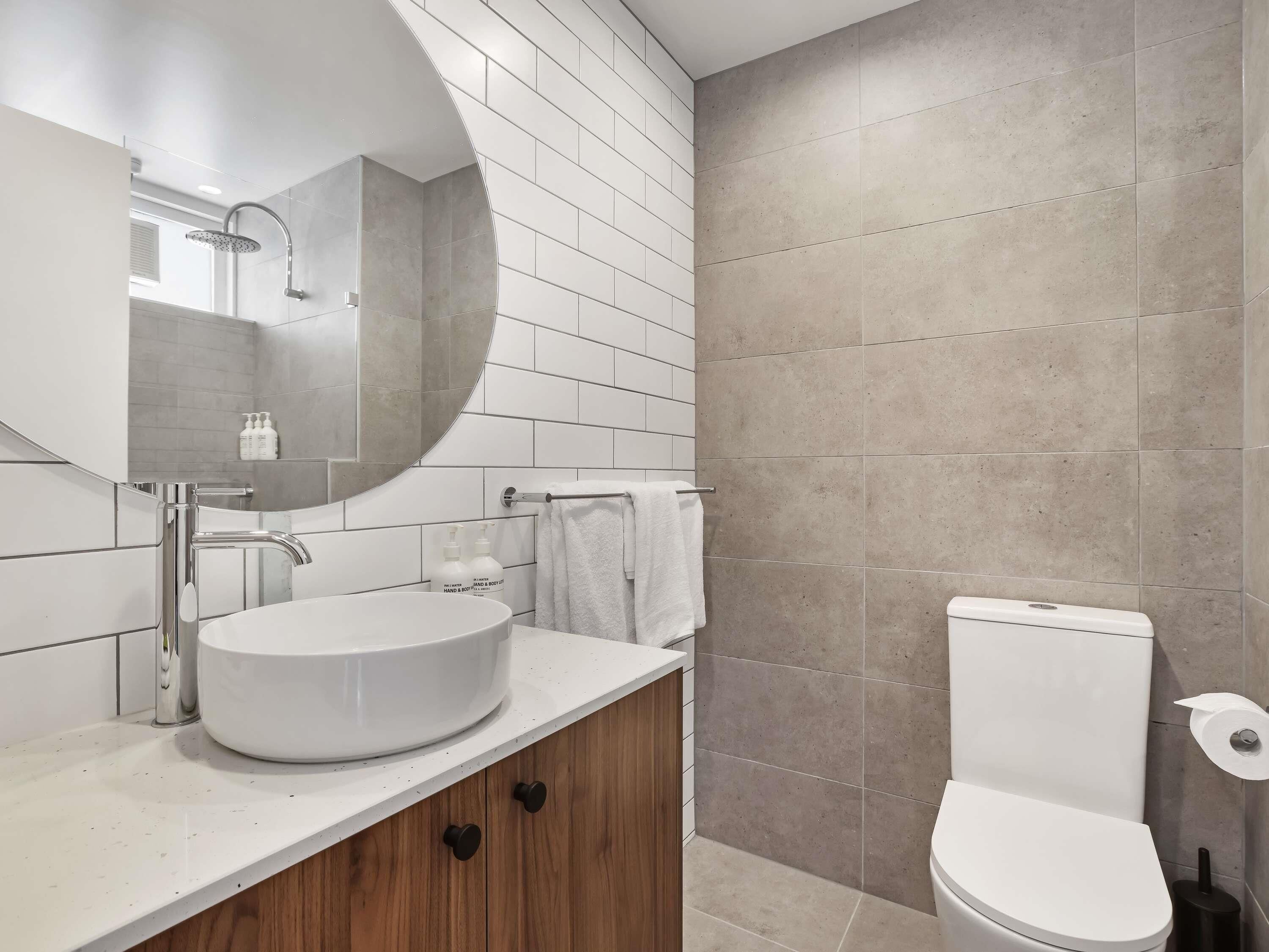 Un baño moderno con un lavamanos blanco, un espejo grande, un cabezal de ducha y un inodoro.