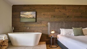 A modern bathroom with a freestanding bathtub, a bedside table with a lamp, and a large bed with pillows. - Mercure Barossa Valley (Tanunda)