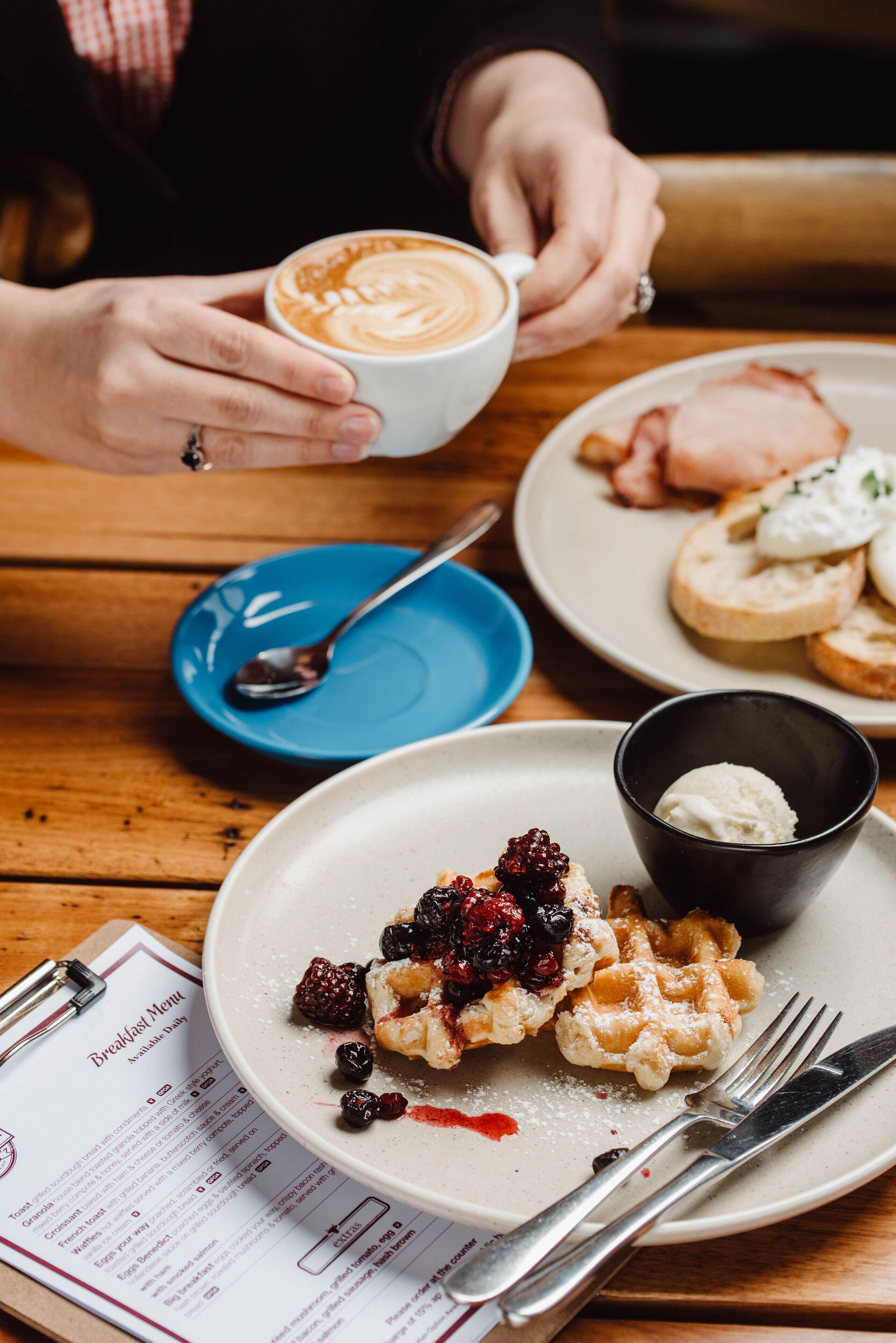 Une table en bois dressée pour le petit-déjeuner, avec des gaufres, des fruits rouges et une tasse de café.