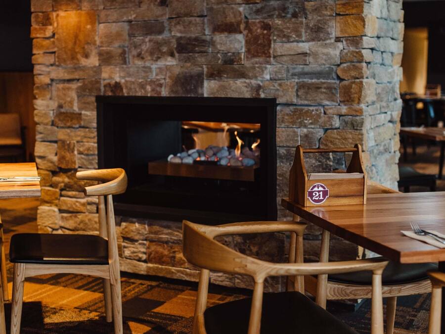 A cozy restaurant interior with a stone fireplace, wooden chairs, and a table with a placemat.