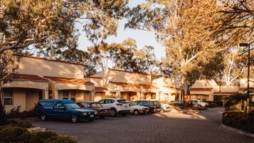 A row of parked cars in front of a building with a tiled roof and beige walls.