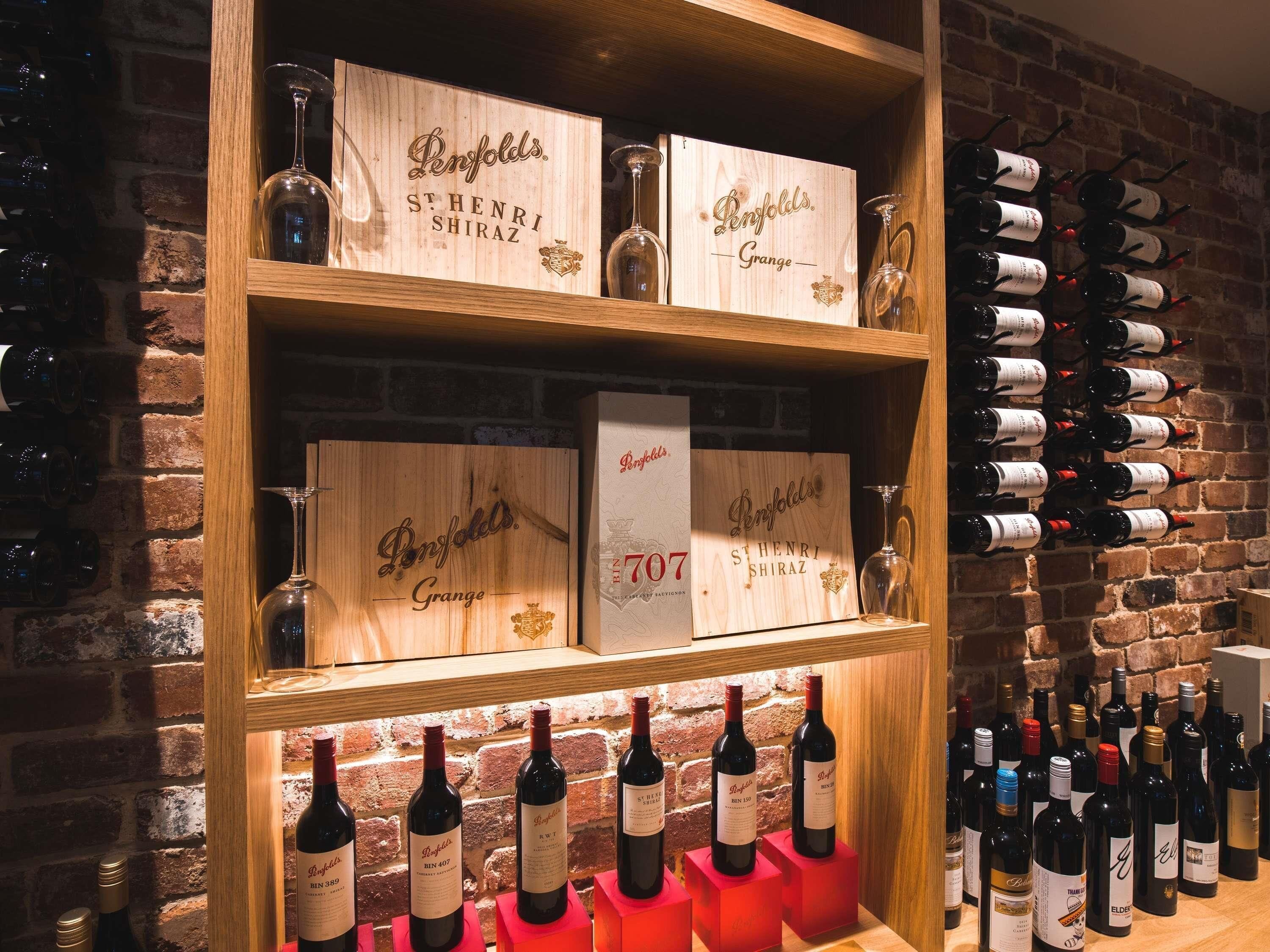 A wine rack with bottles and wooden boxes labeled 'Penfolds' and 'St. Henri Shiraz.'