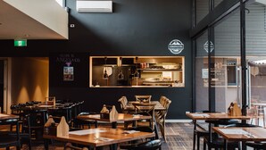 A restaurant interior with multiple tables and chairs, hanging pendant lights, and a black wall with a sign. - Mercure Barossa Valley (Tanunda)