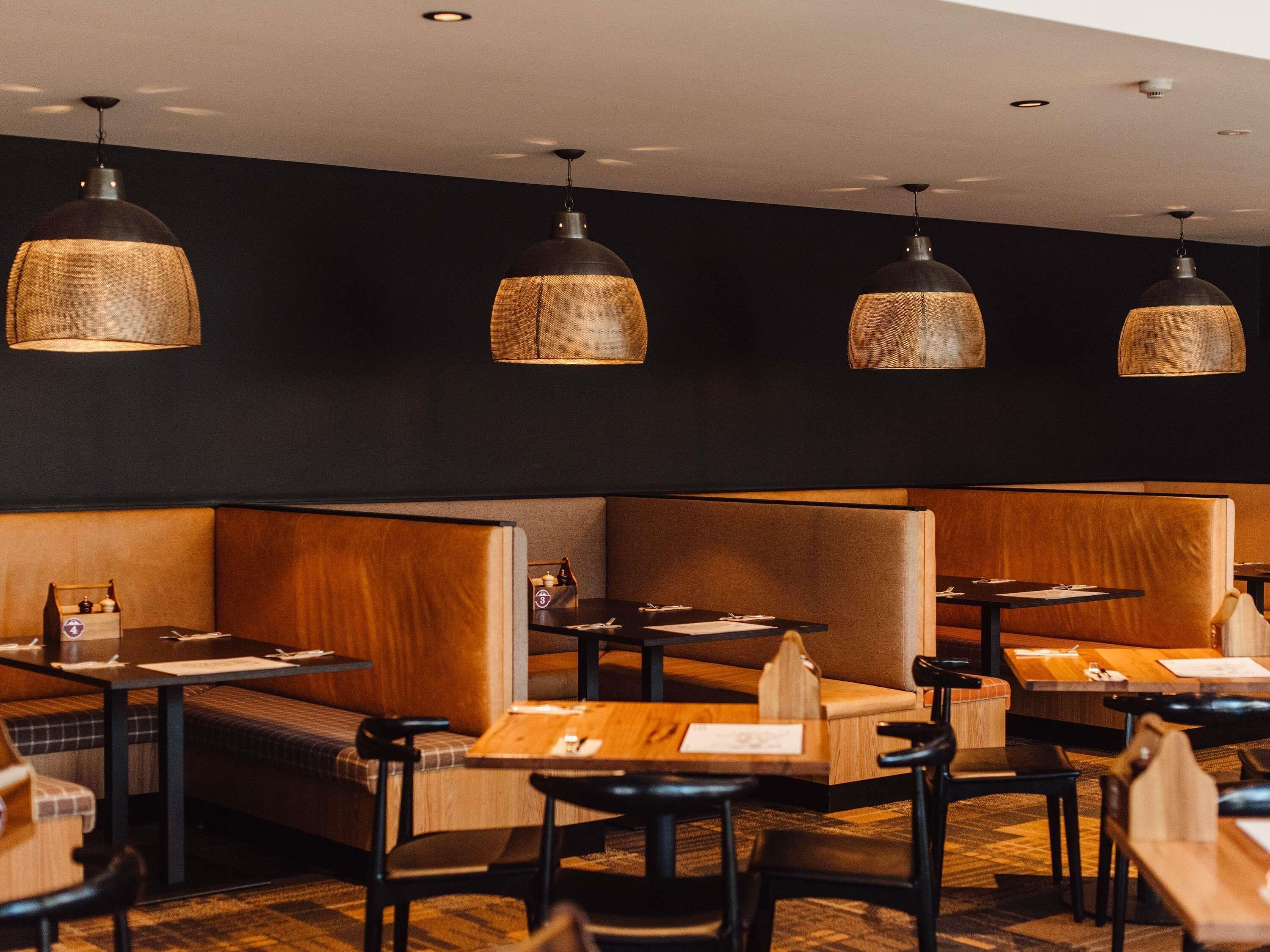A restaurant interior with booth seating, tables, and hanging pendant lights.