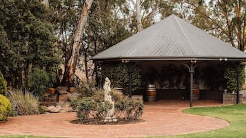 A gazebo with a tiled roof, surrounded by a brick pathway, and a statue in the center.