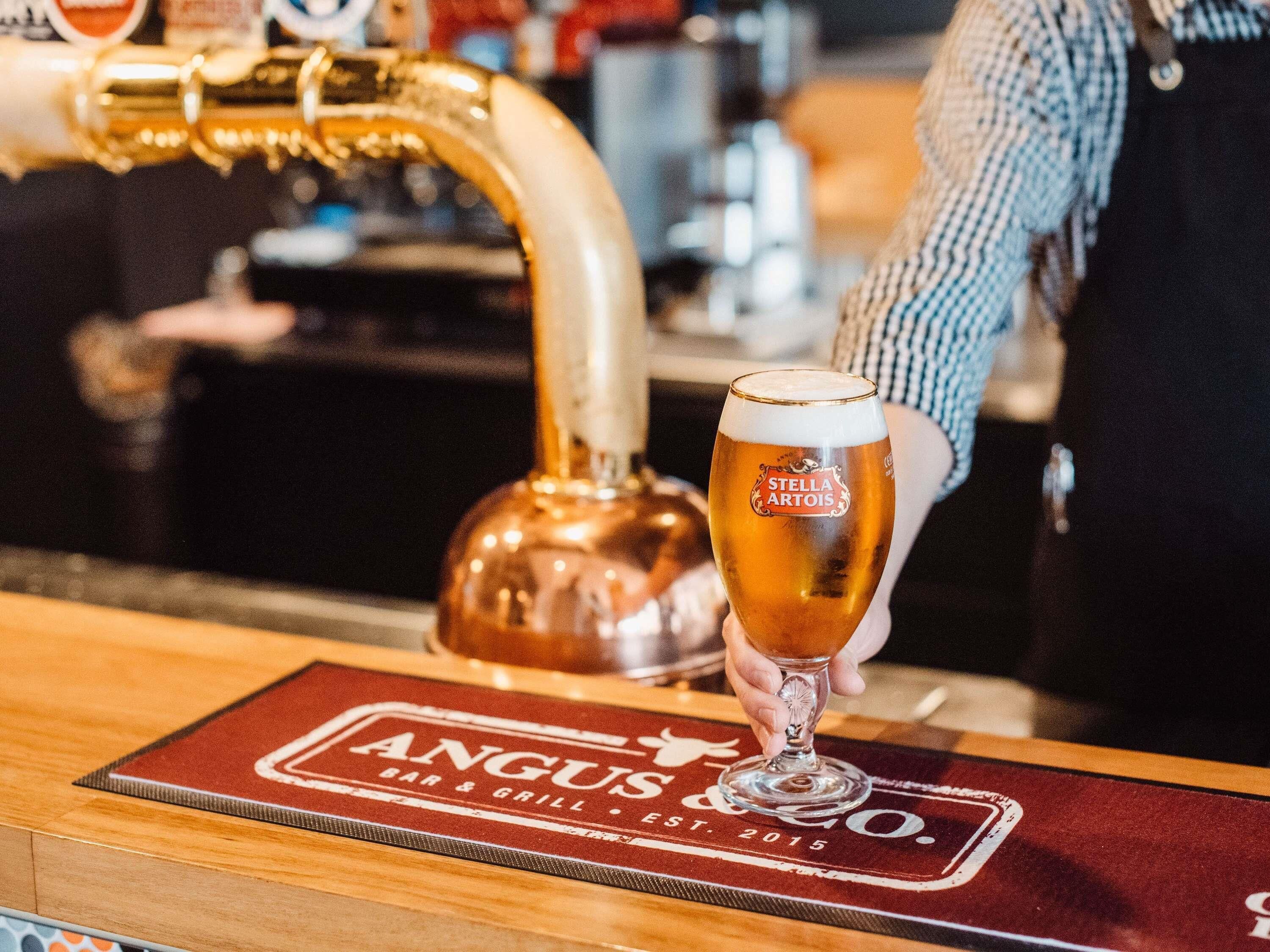 Un grifo vertiendo cerveza en un vaso con la etiqueta 'Stella Artois' en un bar llamado 'Angus & Grill'.