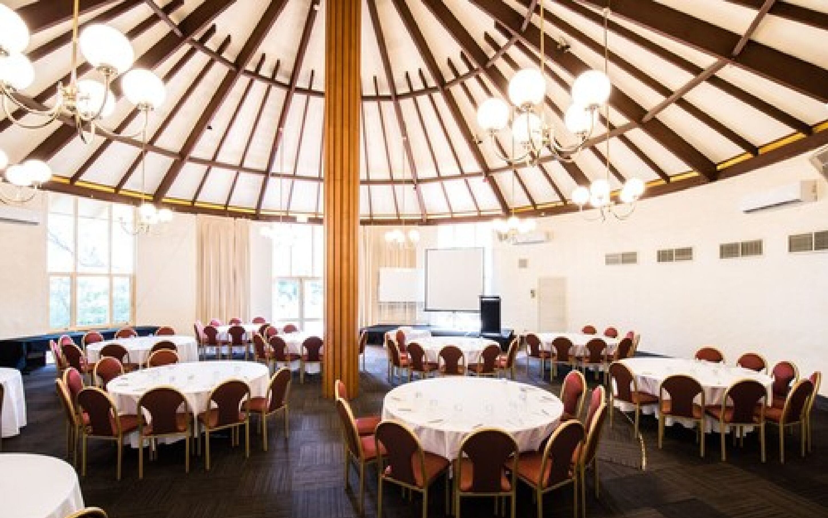 A large, circular room with round tables and chairs, a high wooden ceiling with chandeliers, and large windows.