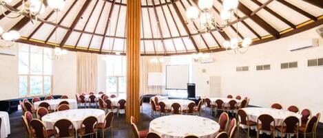A large, circular room with round tables and chairs, a high wooden ceiling with chandeliers, and large windows.