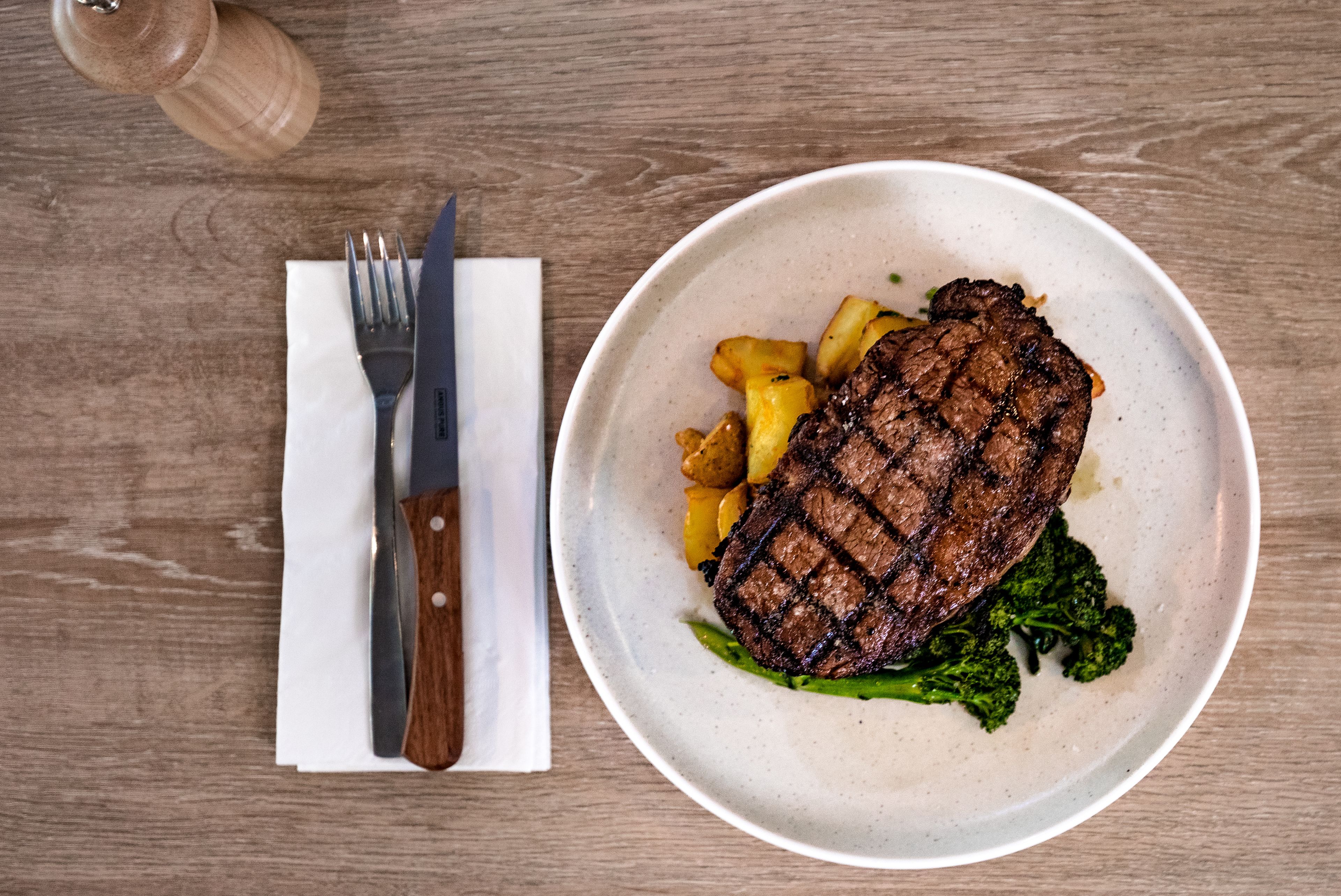 Une assiette contenant un steak grillé, des pommes de terre rôties et des brocolis, le tout posé sur une table en bois.