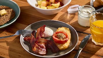 A breakfast setting with a plate of eggs, bacon, and tomato on toast, a bowl of fruit, and a glass of orange juice.