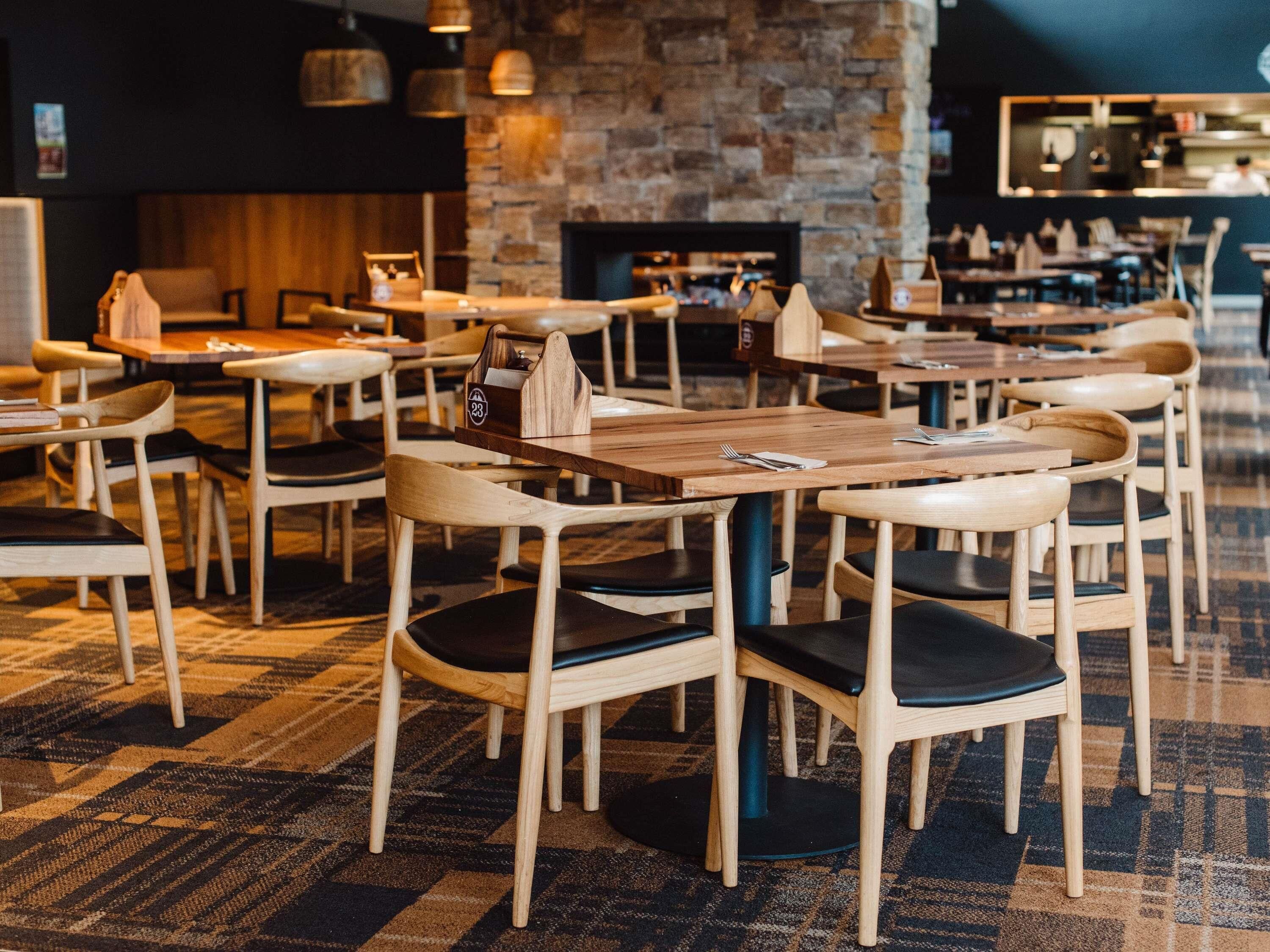 L’intérieur d’un restaurant avec des tables et des chaises en bois, un mur en pierre et une cheminée.
