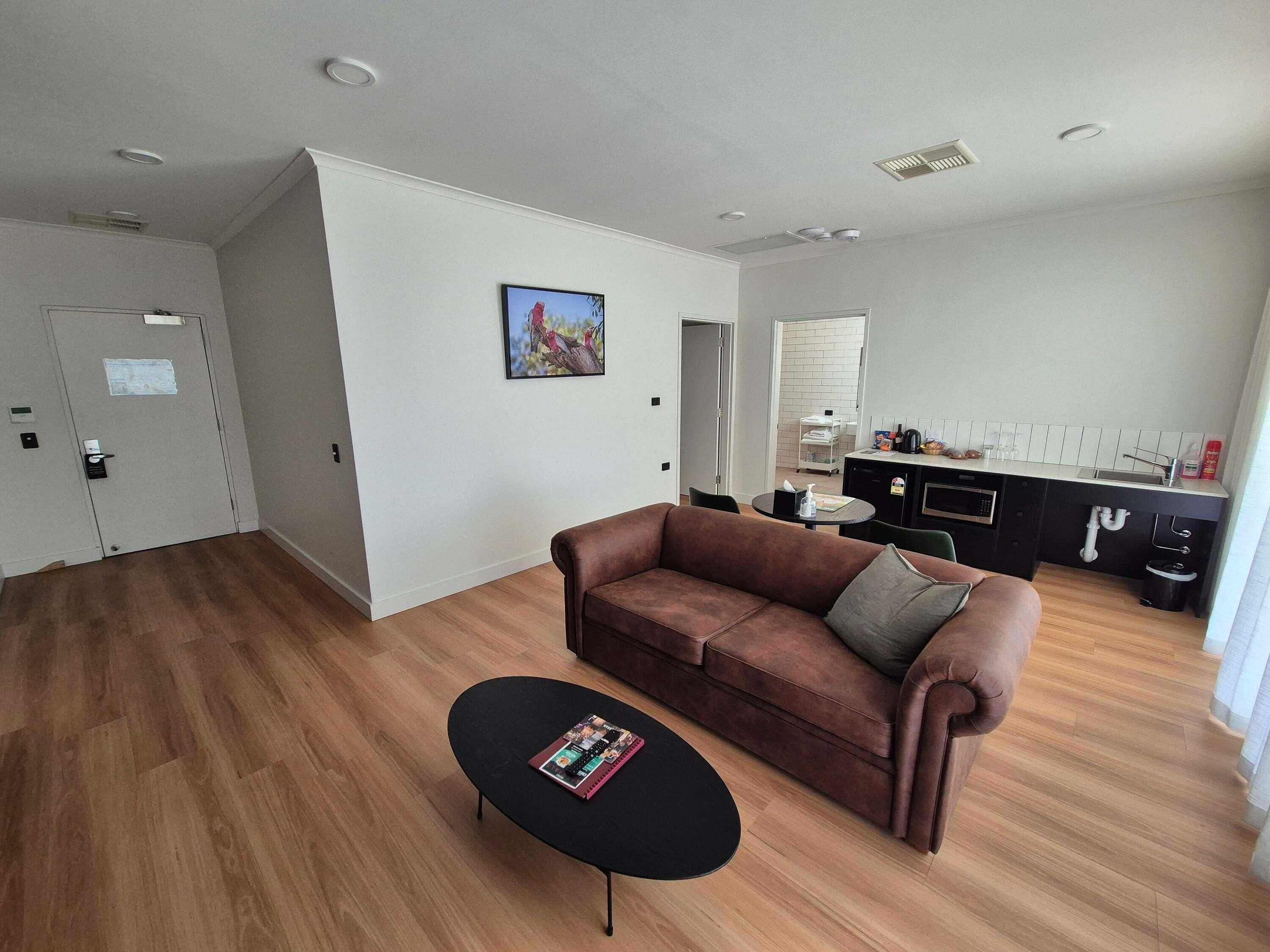 A modern living room with a brown sofa, a black coffee table, and a kitchen area in the background.