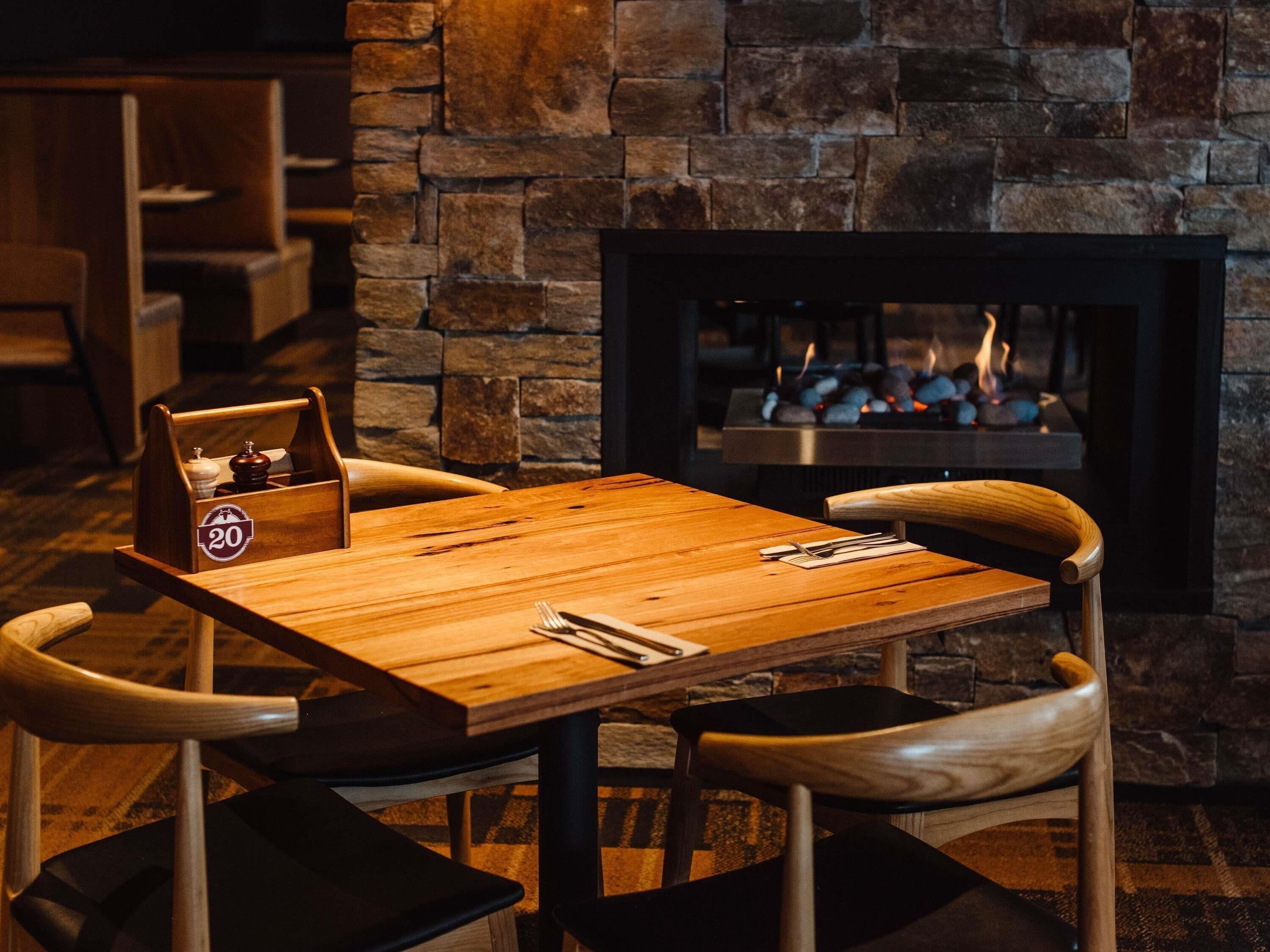 A cozy dining area with a wooden table and chairs, a stone wall, and a fireplace with a fire.