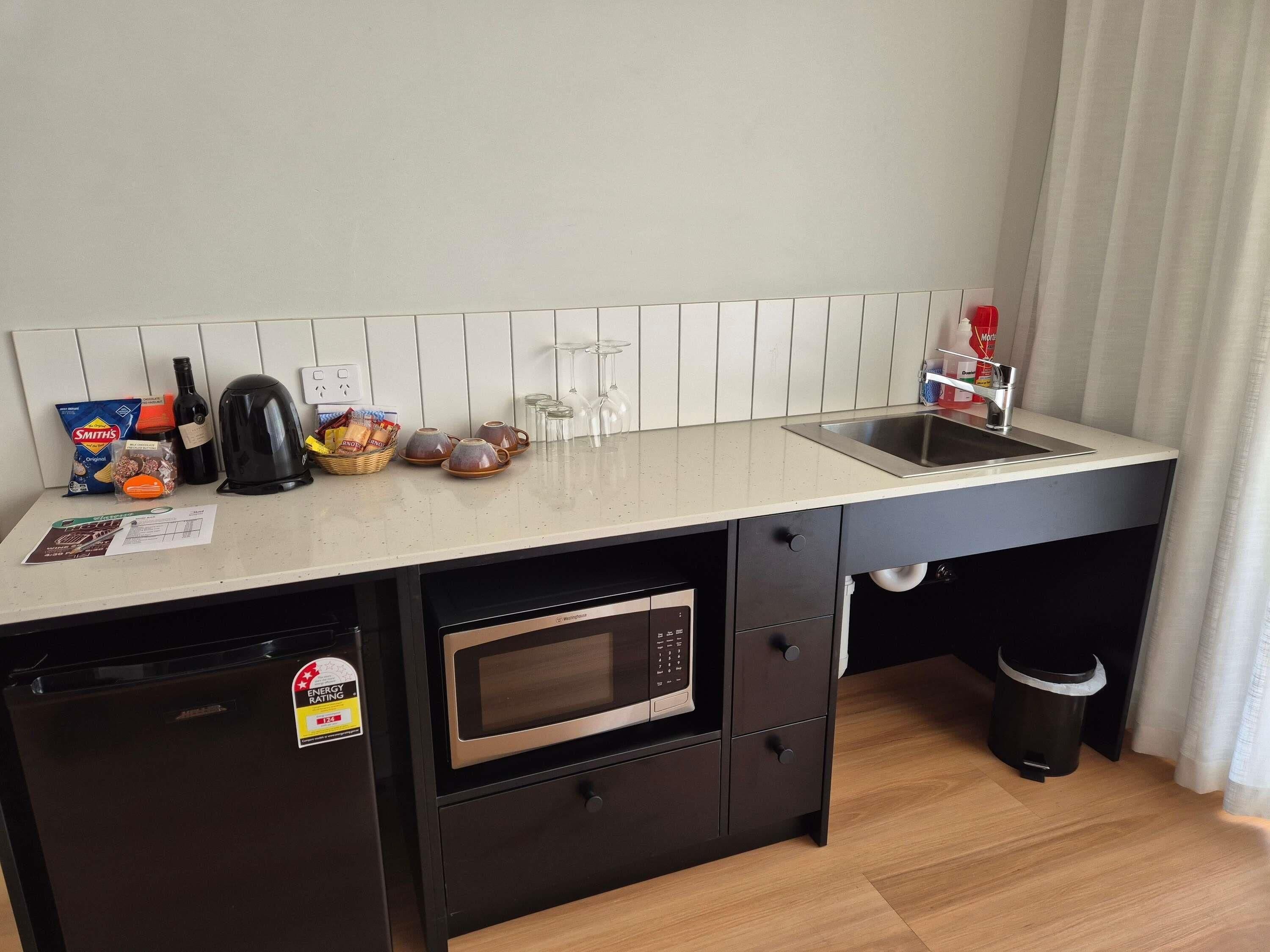 Una kitchenette compacta equipada con microondas, cafetera, hervidor y pileta.