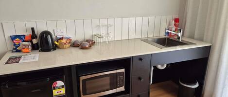 Una kitchenette compacta equipada con microondas, cafetera, hervidor y pileta.