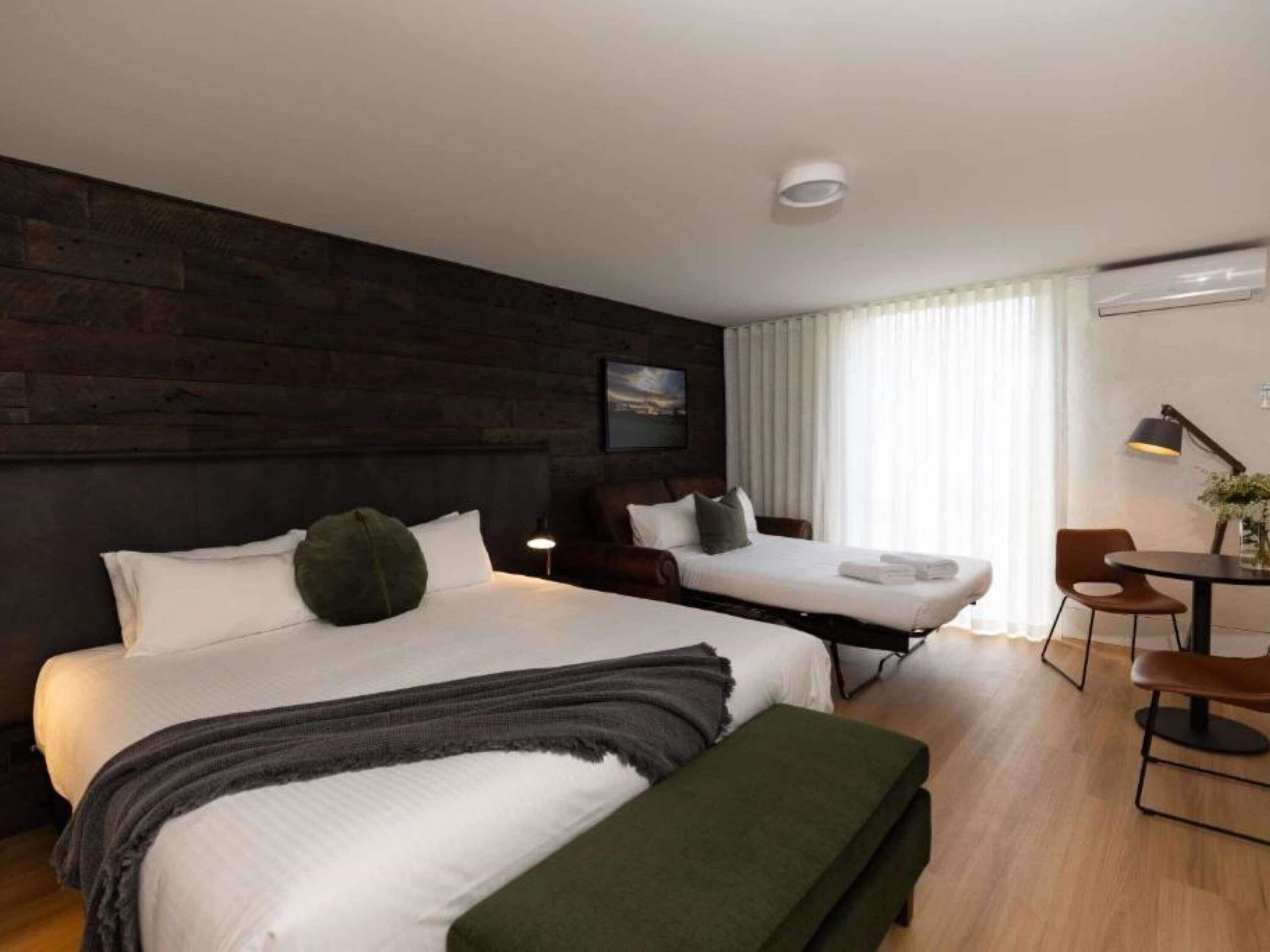 Une chambre d’hôtel avec deux lits, un bureau, une chaise, une lampe et une fenêtre avec des rideaux.