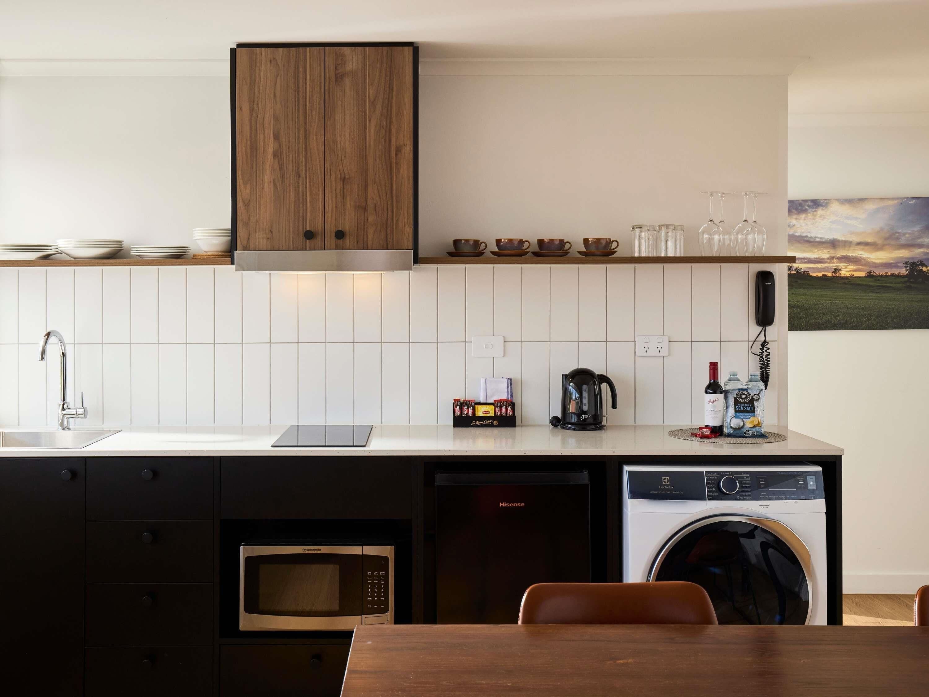 Une cuisine moderne avec des meubles en bois, un crédence carrelée de couleur blanche, un évier, une machine à café, un four à micro-ondes, un lave-vaisselle et une table avec des chaises.