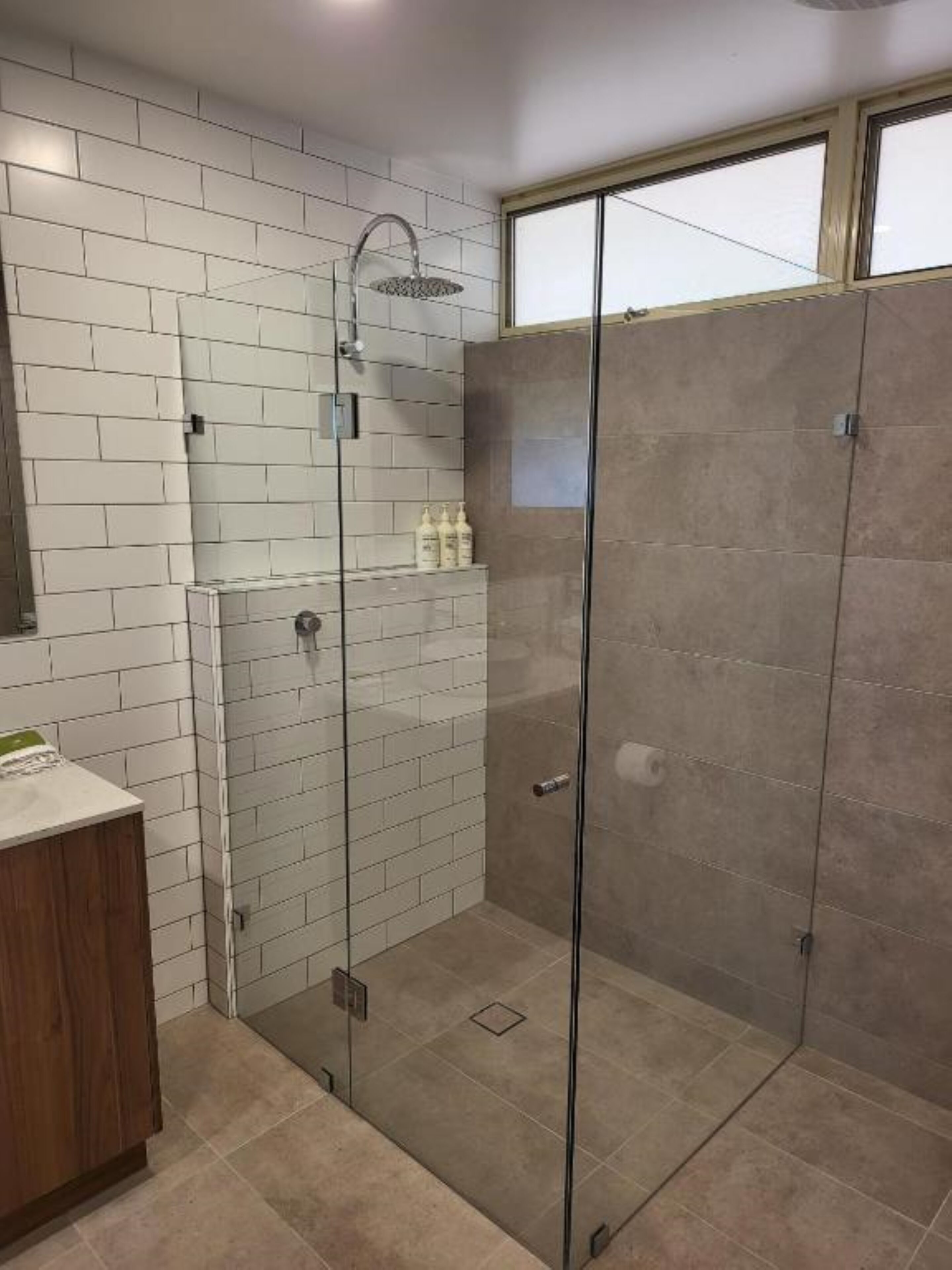 A modern bathroom with a glass-enclosed shower, white tiled walls, and a wooden vanity.