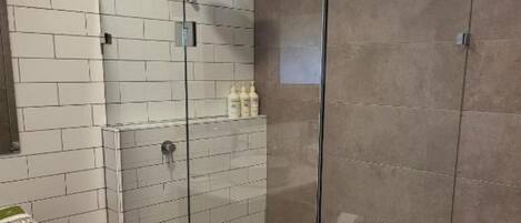 A modern bathroom with a glass-enclosed shower, white tiled walls, and a wooden vanity.