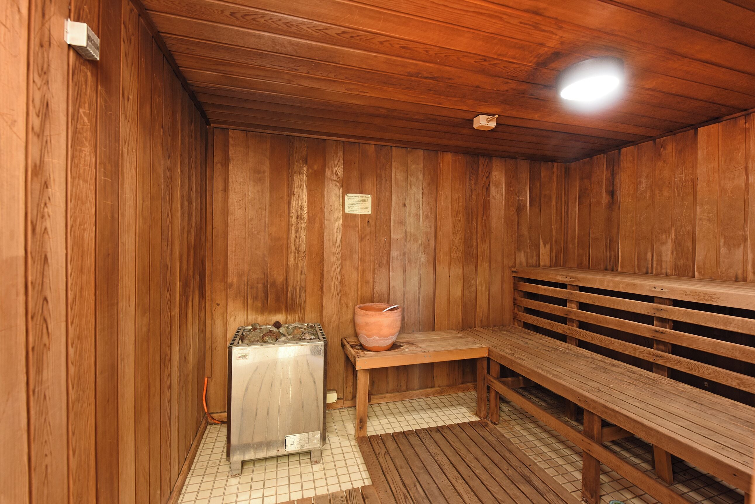 Una sala de sauna con paredes de madera, un banco, un calentador y una olla grande.