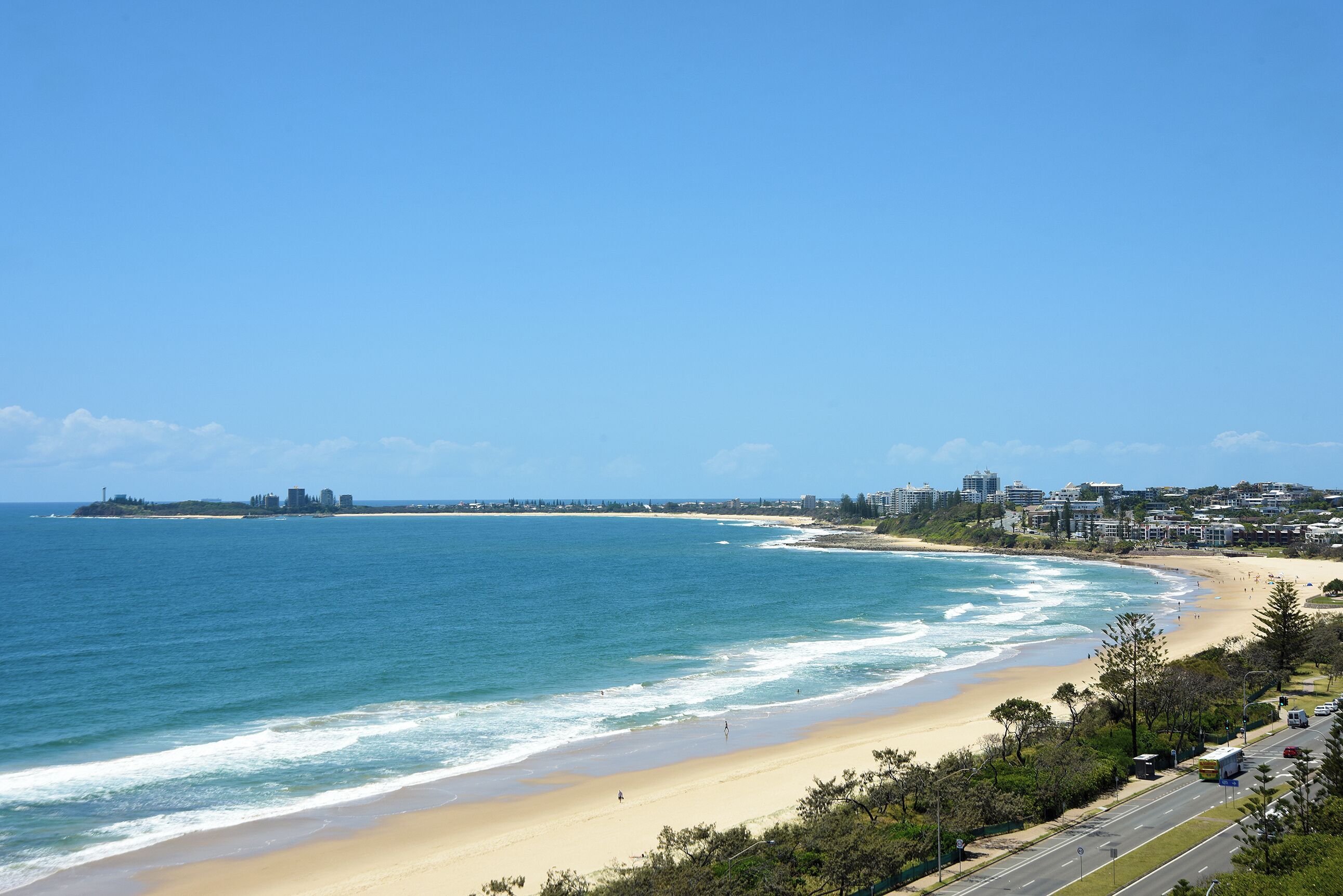 Vista costeira com praia, oceano e edifícios ao longe.