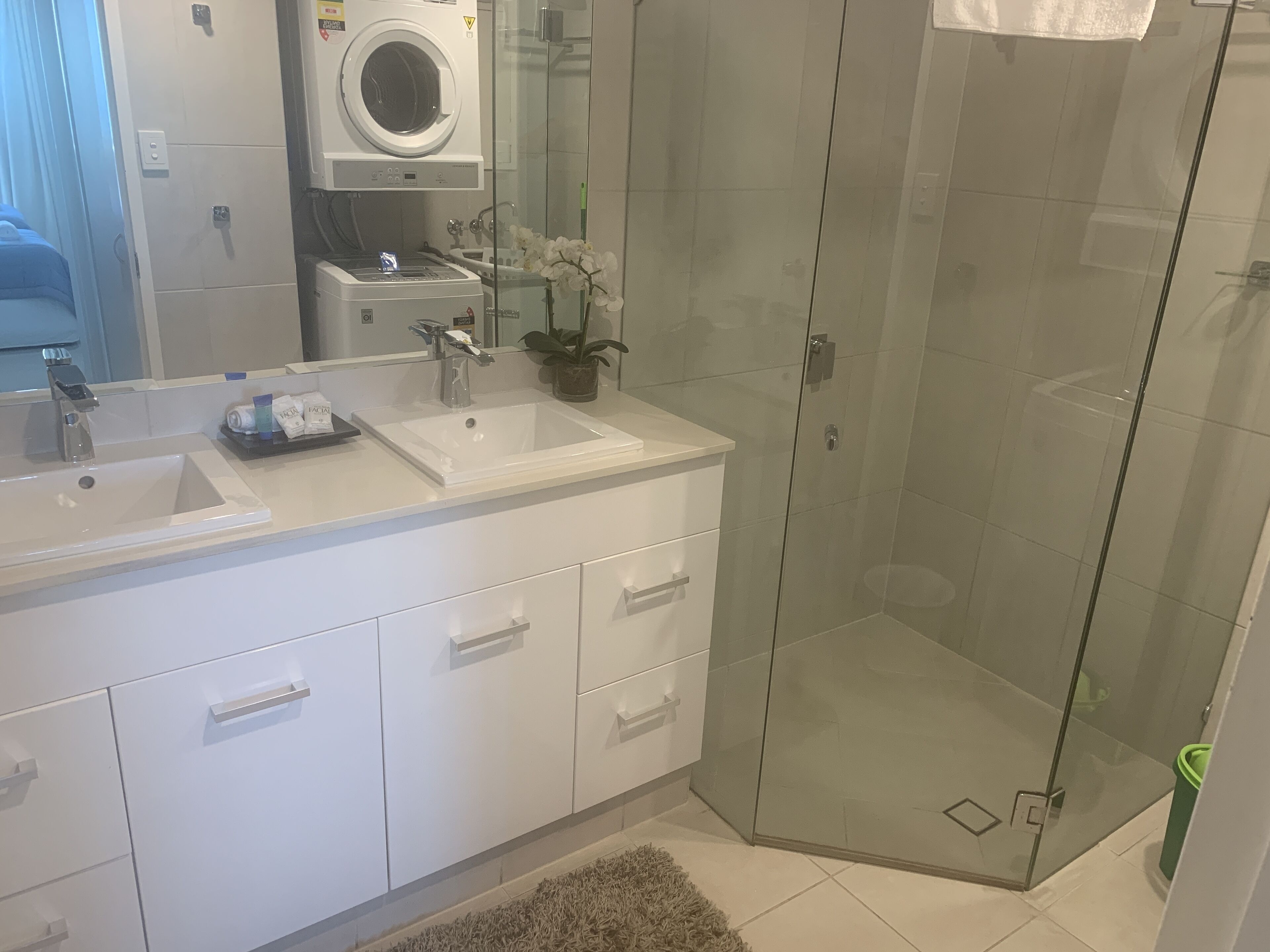 A modern bathroom with a glass-enclosed shower, a built-in washing machine, and a vanity with a sink and mirror.