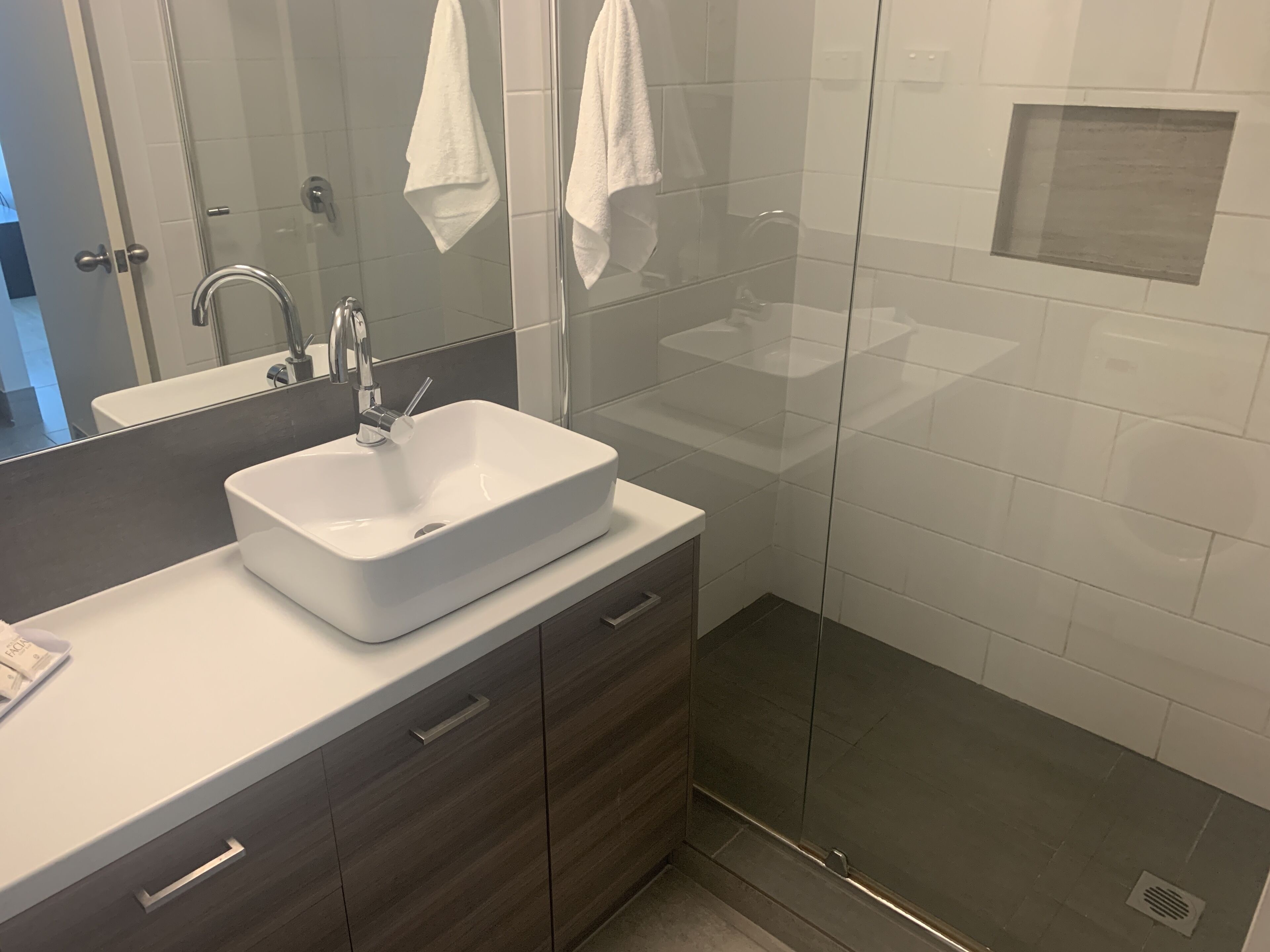 A modern bathroom with a white sink, dark wooden vanity, and a glass shower enclosure.
