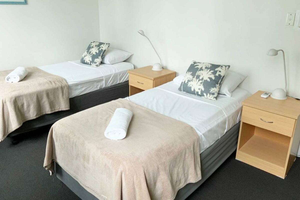 A hotel room with two single beds, each with a bedside table and lamp.