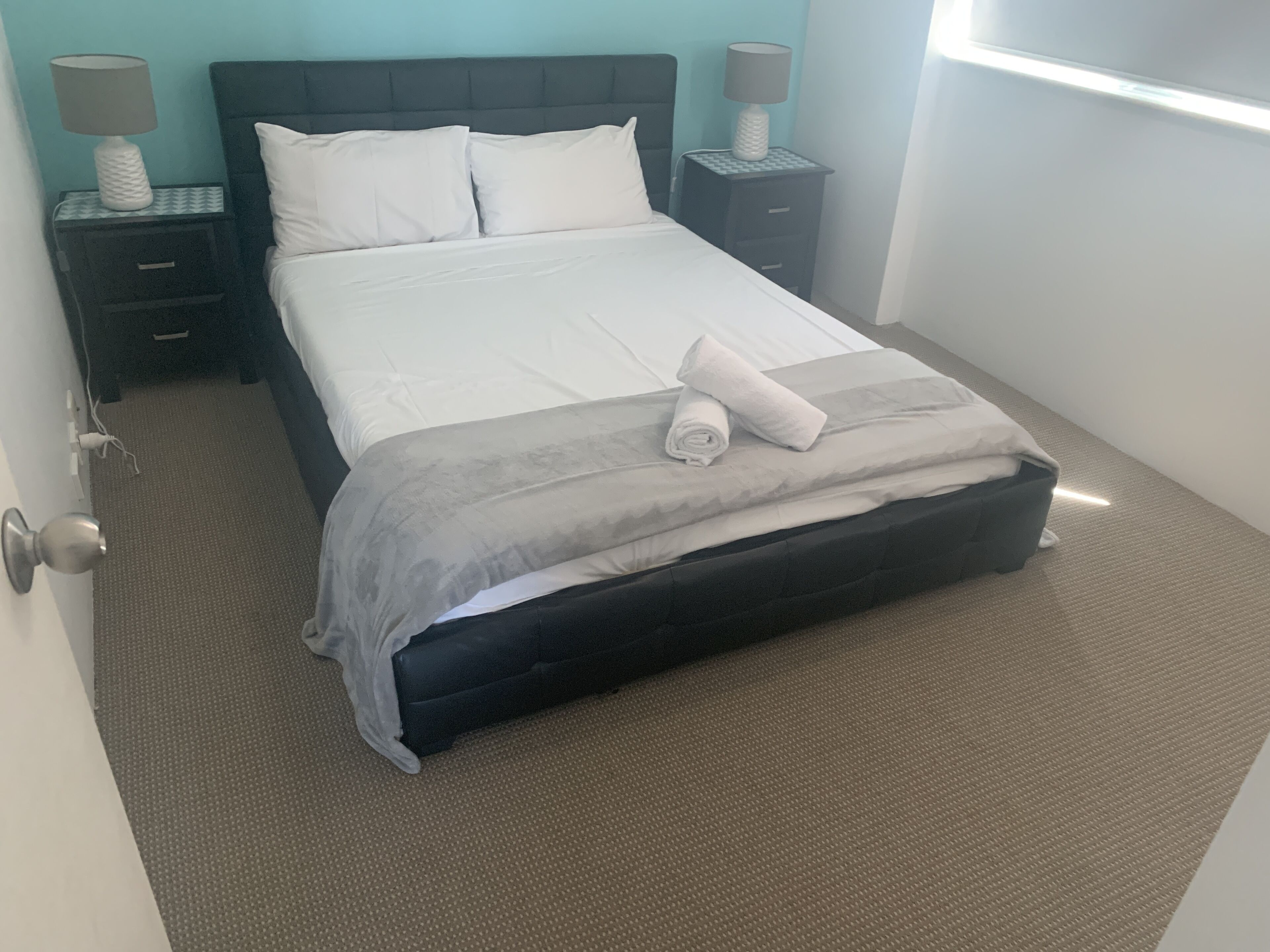A neatly made bed with white linens and a grey throw, two bedside tables with lamps, and a blue wall.