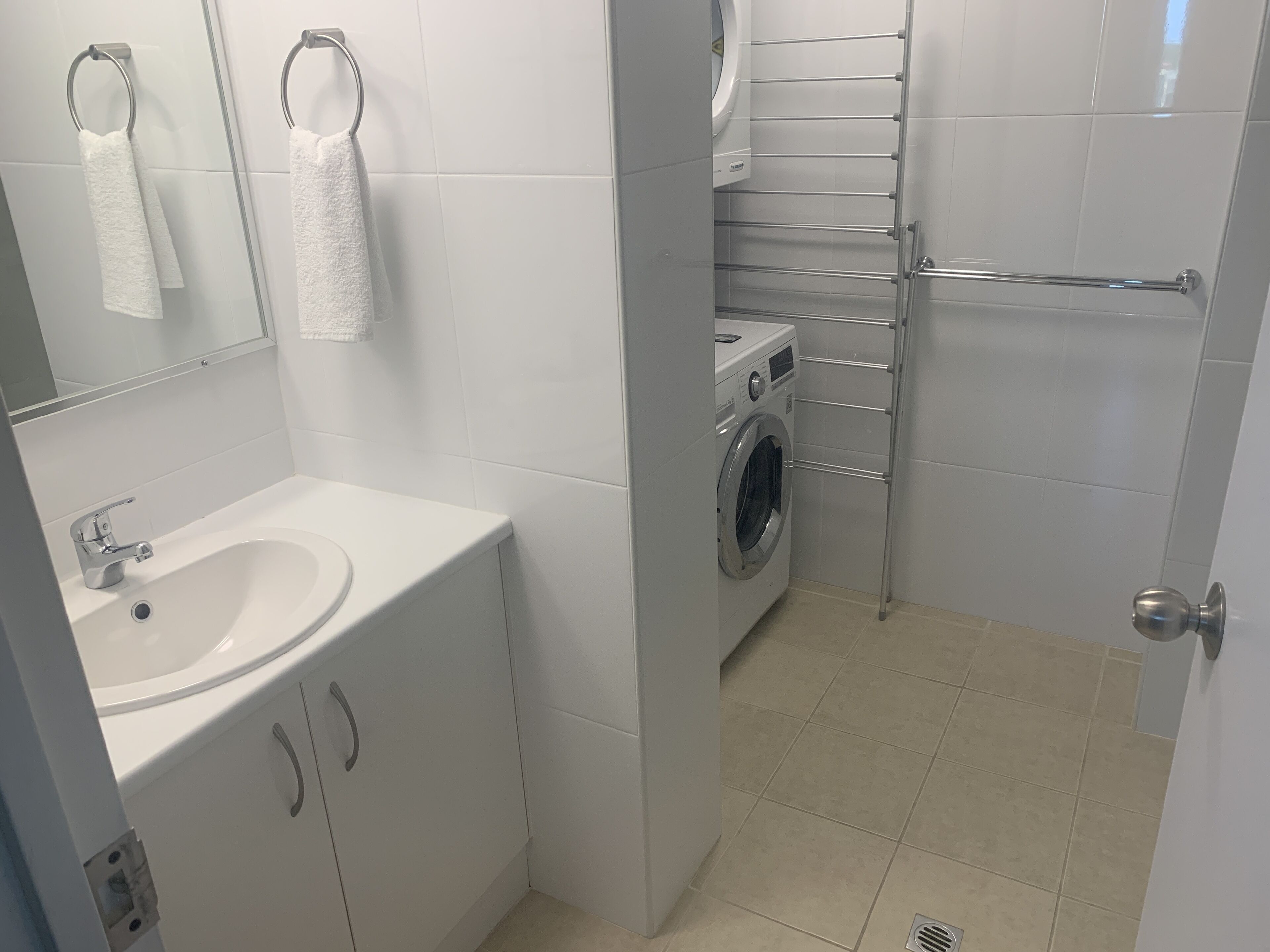 Ett modernt badrum med en vit tvättställ, en spegel, en tvättmaskin och en handduksställning.
