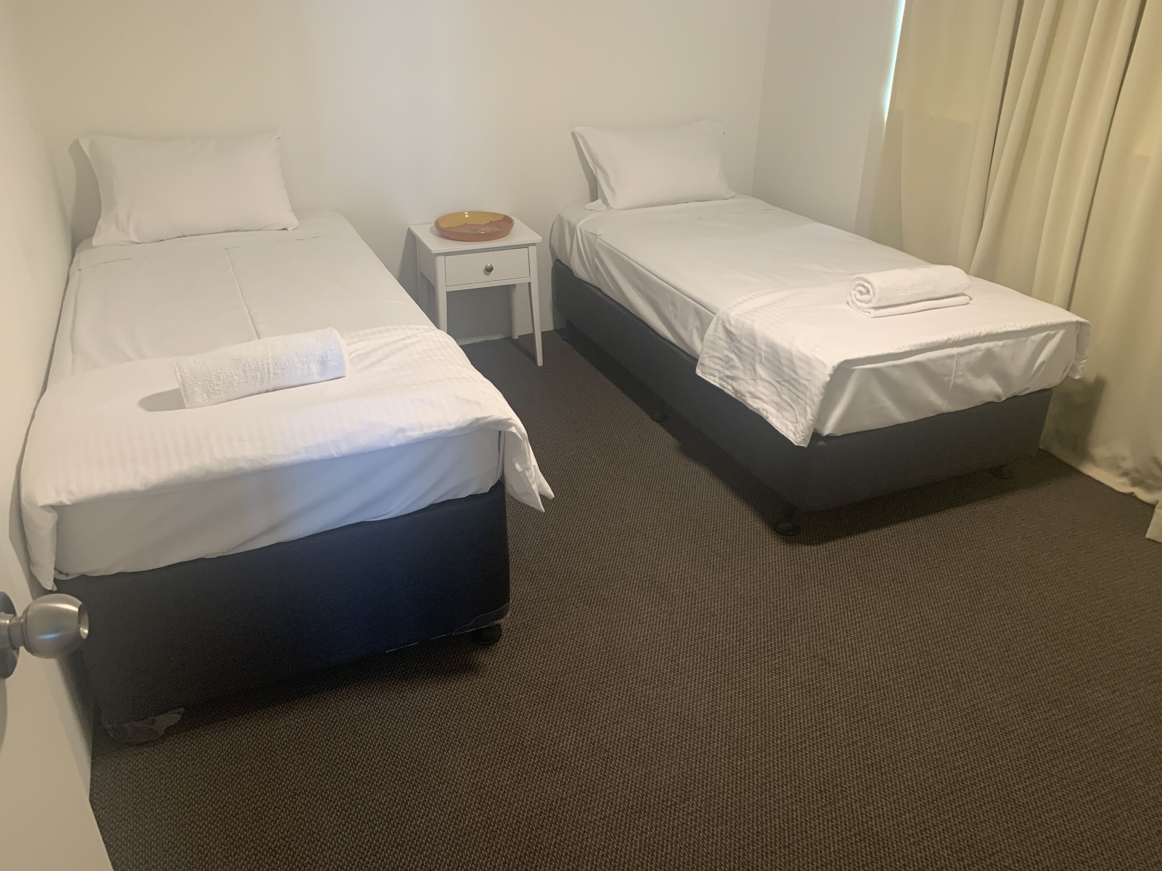 Habitación de hotel con dos camas, una mesita de noche con un bol y suelo alfombrado.