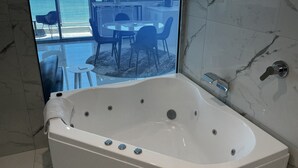 Un bagno moderno con una grande vasca da bagno, una parete rivestita in marmo e vista sull'oceano attraverso ampie finestre.