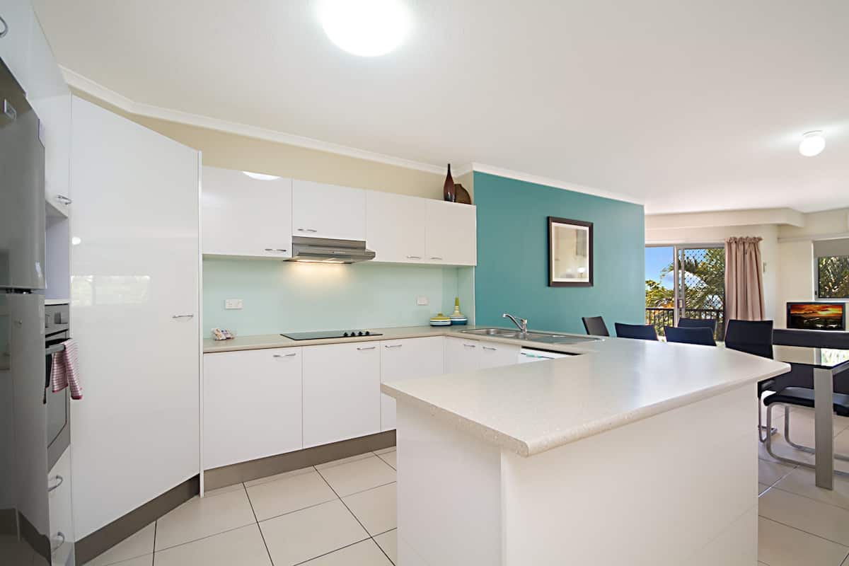 A modern kitchen with white cabinets, a central island, and a dining area with a TV.