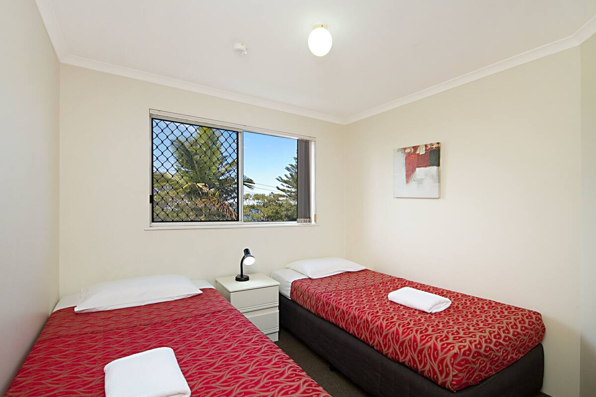 A room with two beds, a window with a view, a nightstand, and a ceiling light.