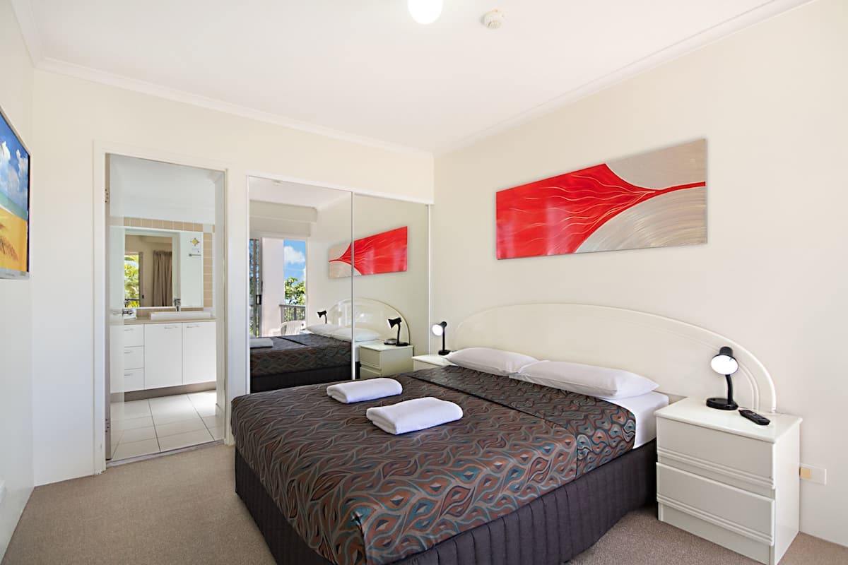 A hotel room with a bed, bedside table, and a mirror.