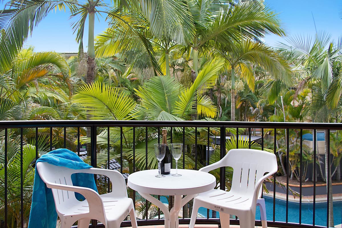 A balcony with a white table and two white chairs, a bottle of champagne, and two glasses.
