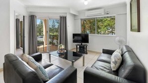 A modern living room with a sofa, a coffee table, a TV, and a balcony with curtains. - Blue Waters Apartments (Labrador)