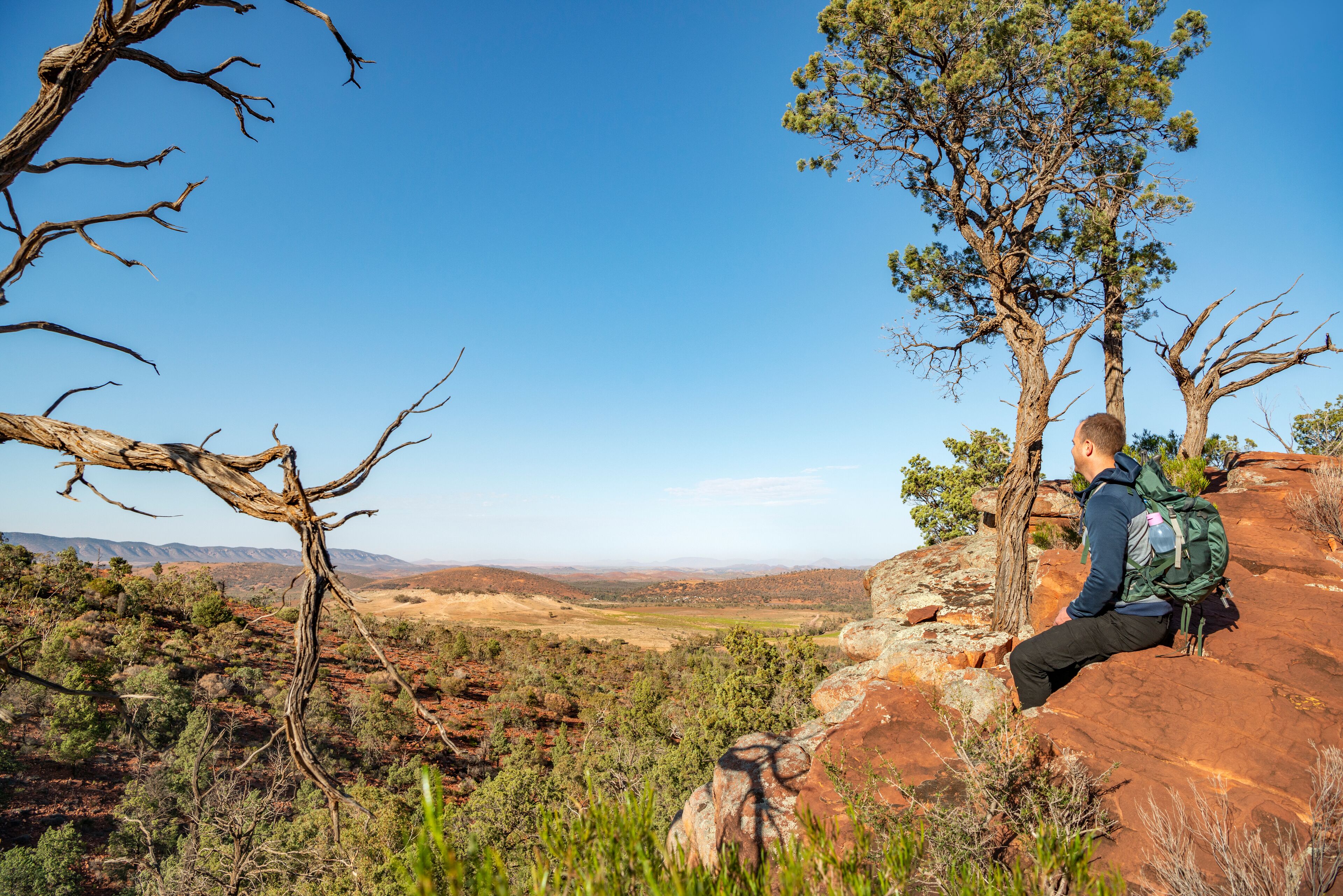 A hiker sitting on a rock with a backpack, overlooking a mountainous landscape.