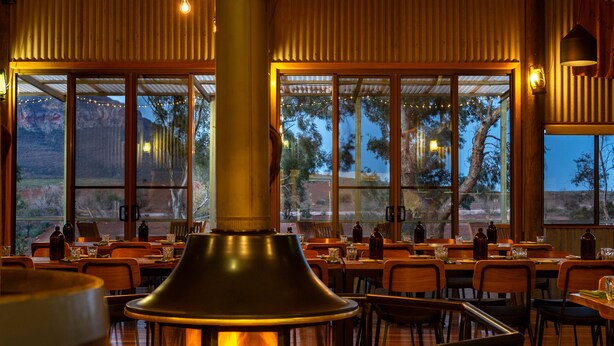 Interior de restaurante con estufa de leña, ventanas amplias y vistas al exterior.