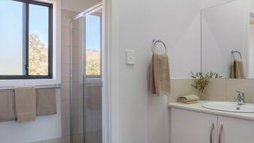 Un baño moderno con ducha de vidrio, un lavabo con espejo y una ventana con vistas al exterior.