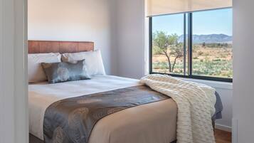 A bedroom with a bed, a ceiling fan, a window with a view of the desert, and an air conditioning unit.