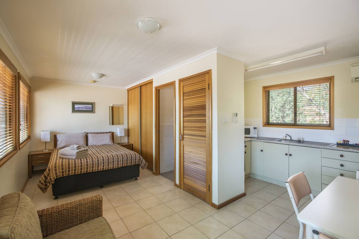 A bedroom with a bed, bedside table, and a window with blinds.