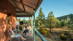 Un espacio al aire libre cubierto con terraza de madera, sillas de metal y vista a un paisaje boscoso.