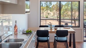 Una cocina moderna con armarios blancos, un ventanal con vista al desierto y una zona de comedor con dos sillas.